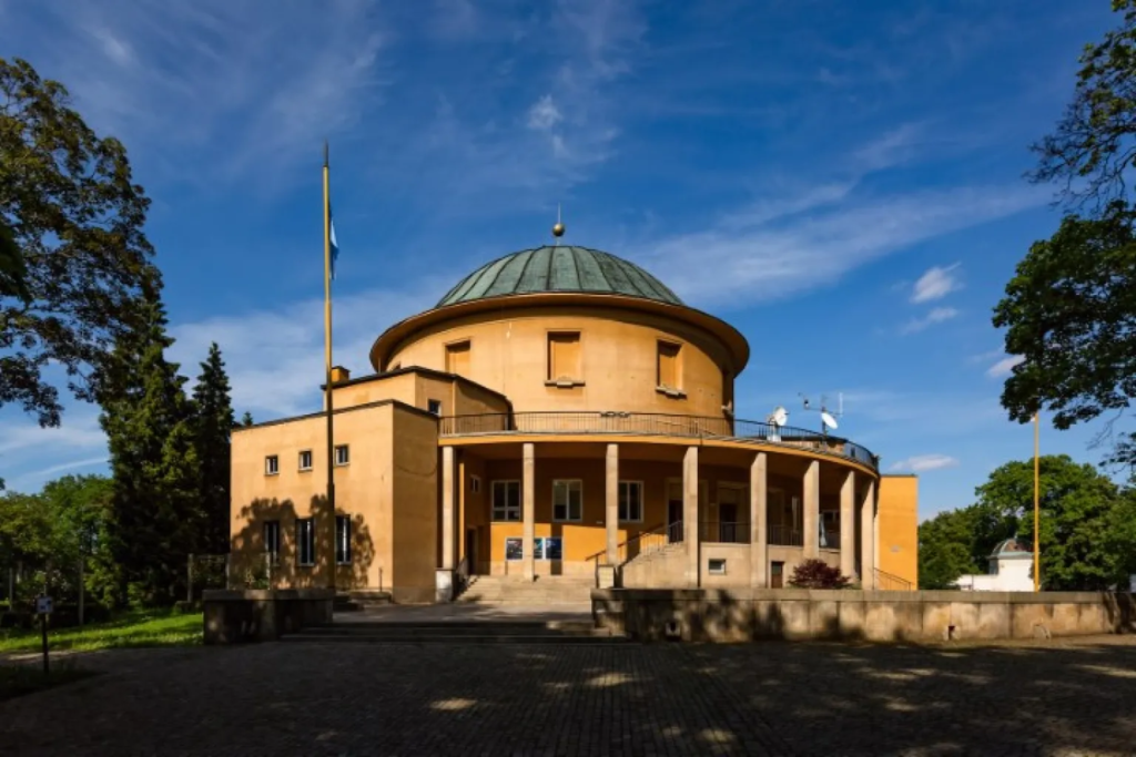 A round orange Planetarium building surrounded with trees standing in a park called Stromovka